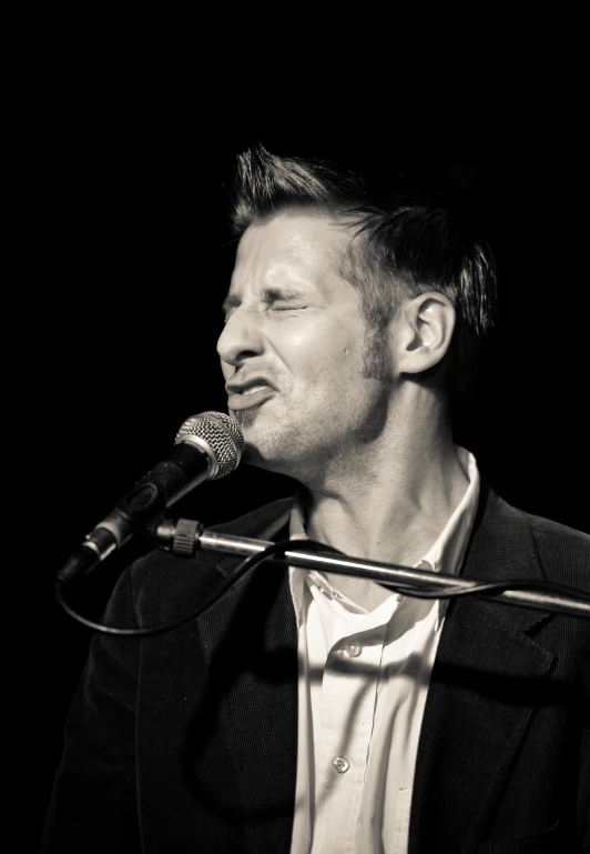 a man singing into a microphone with a black and white background