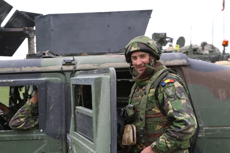 a smiling soldier wearing camouflage near his vehicle