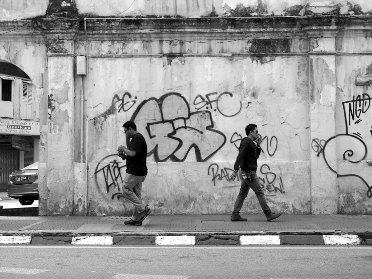 two men walking along side a concrete building with graffiti all over it