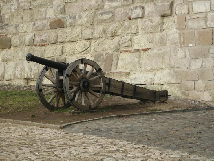 a wooden cannon in front of a wall on a stone street