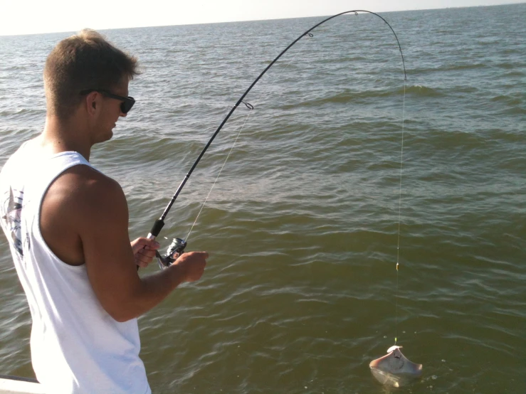 man standing in water, holding fishing rod with small fish nearby