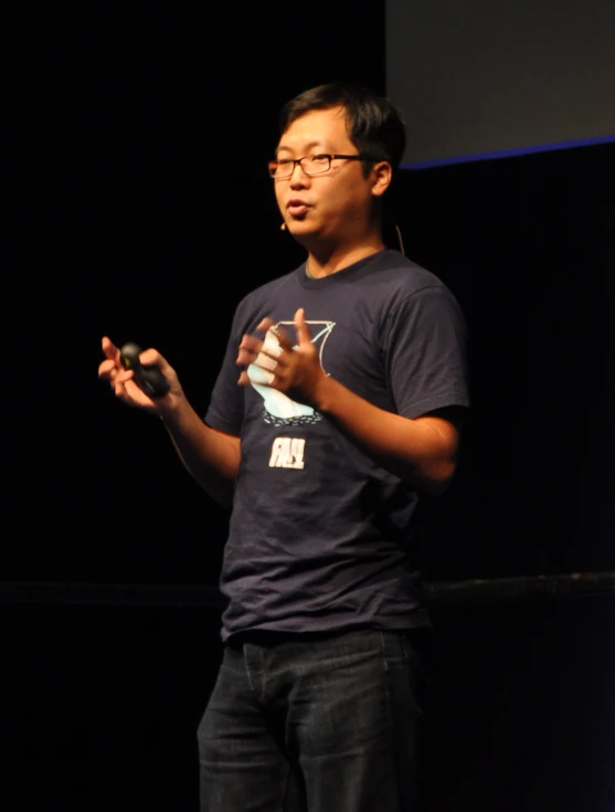 an asian man standing in front of a screen holding his hands
