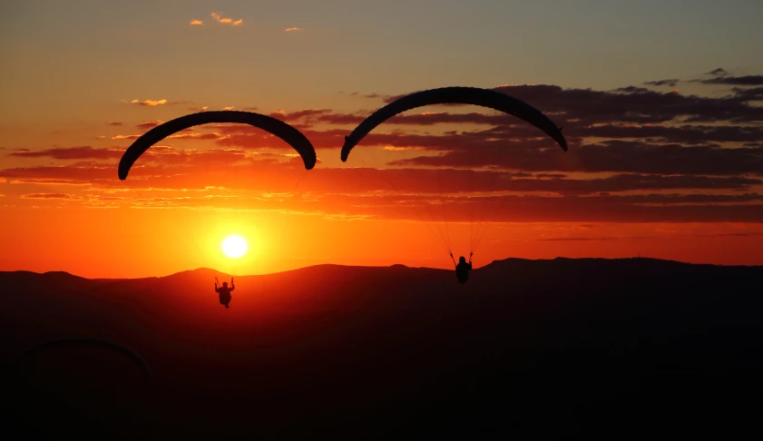 two parasails flying above a mountain during sunset