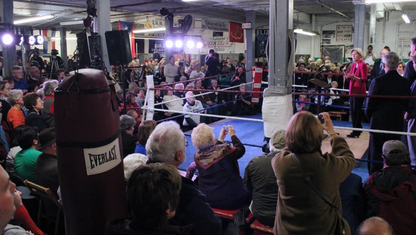 an audience gathers around a boxing ring in the middle of a gym