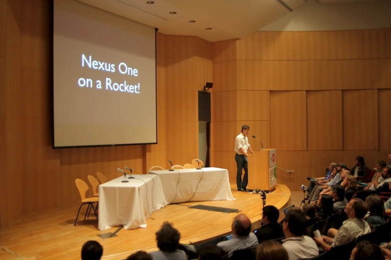 a man giving a presentation on a screen and people seated in chairs