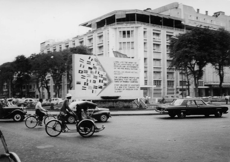 old cars, motorcycles and bikes travel along a street