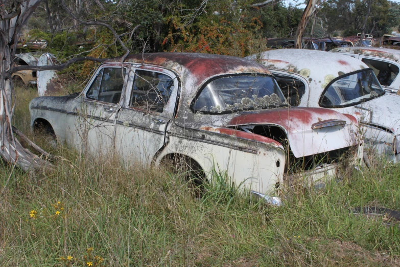 an old rusted car is sitting in the middle of a grassy field