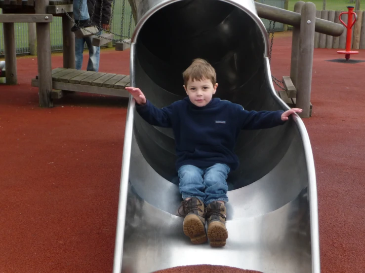 a small boy sits in the metal slide at a playground