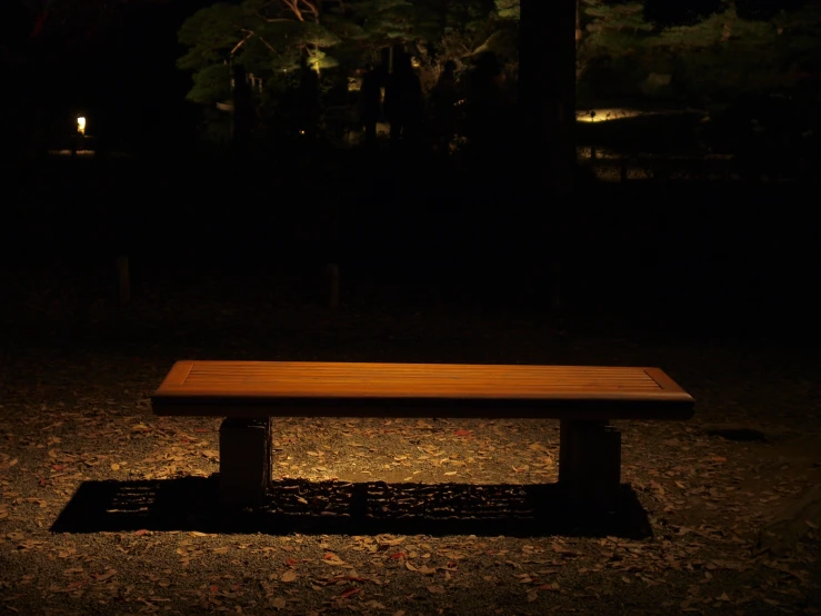 a wooden bench in the dark, casting a shadow