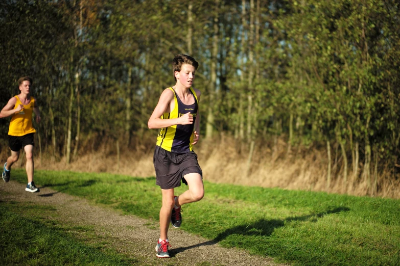 two people running down a dirt path in the woods