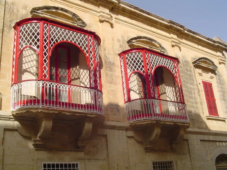 two balconies with red and white shutters on an old building