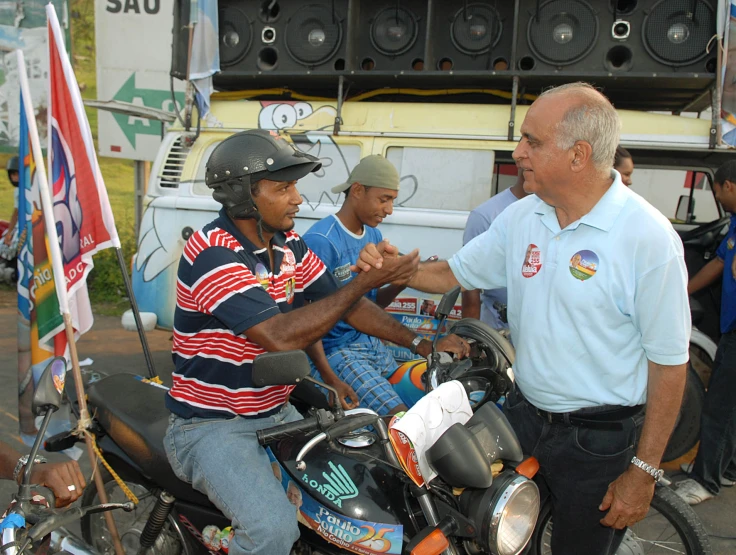 two men are talking on motorcycles near a man holding an umbrella