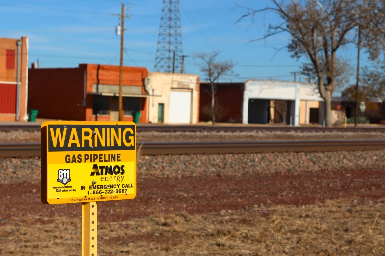 yellow and black warning sign on post next to railroad tracks