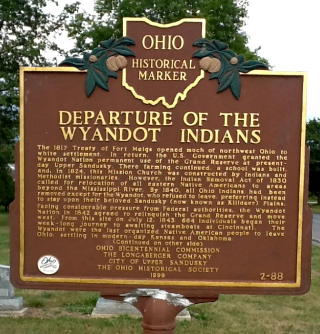 an old marker stands beside a grass - covered cemetery