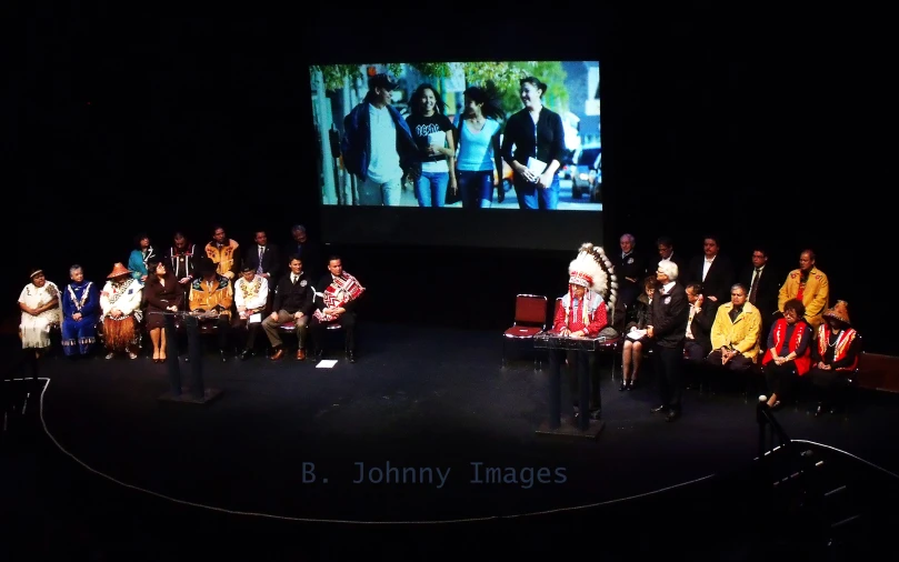 a group of people sit on a stage with one on the stage speaking