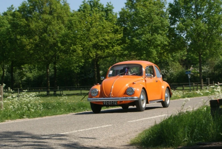 an orange classic car on the road with trees in the background