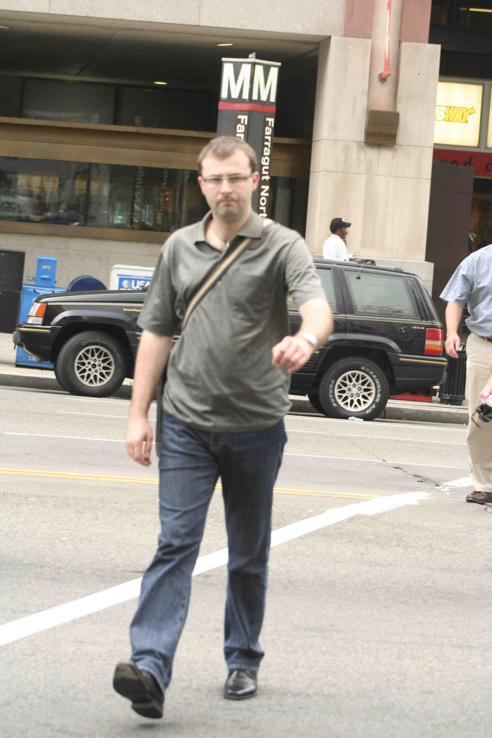 man walking down the street, while cars are parked nearby