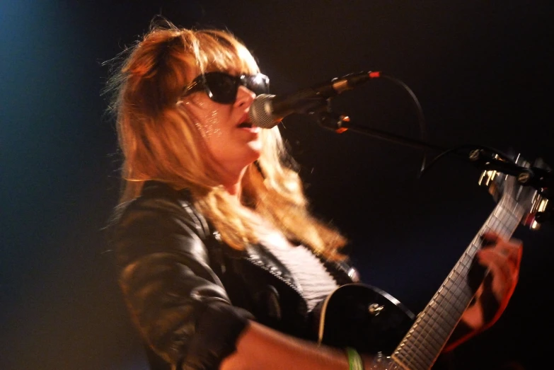 a woman in black jacket holding guitar on stage