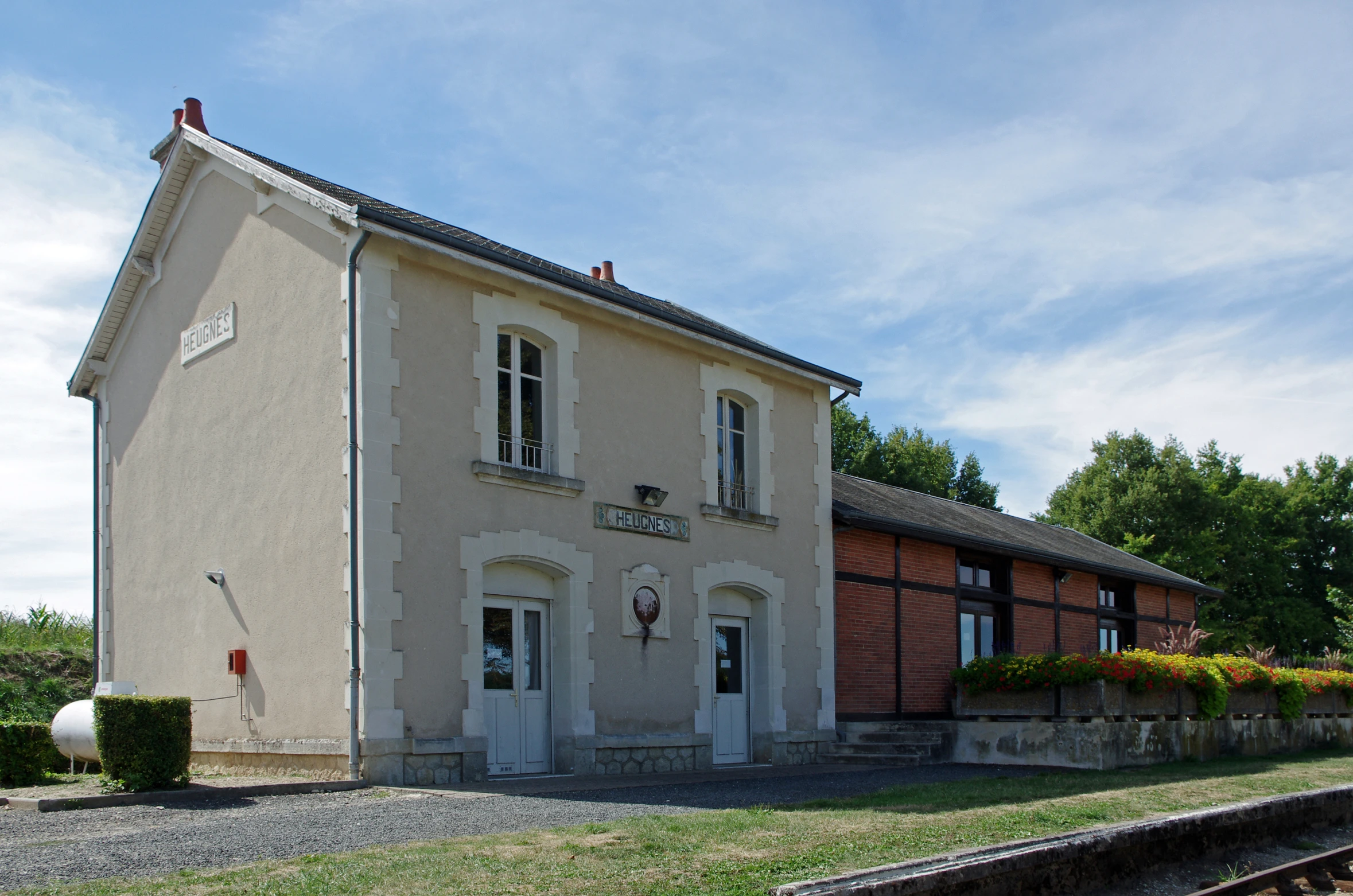 a home is on a grassy plot that sits behind a row of trees and a set of train tracks