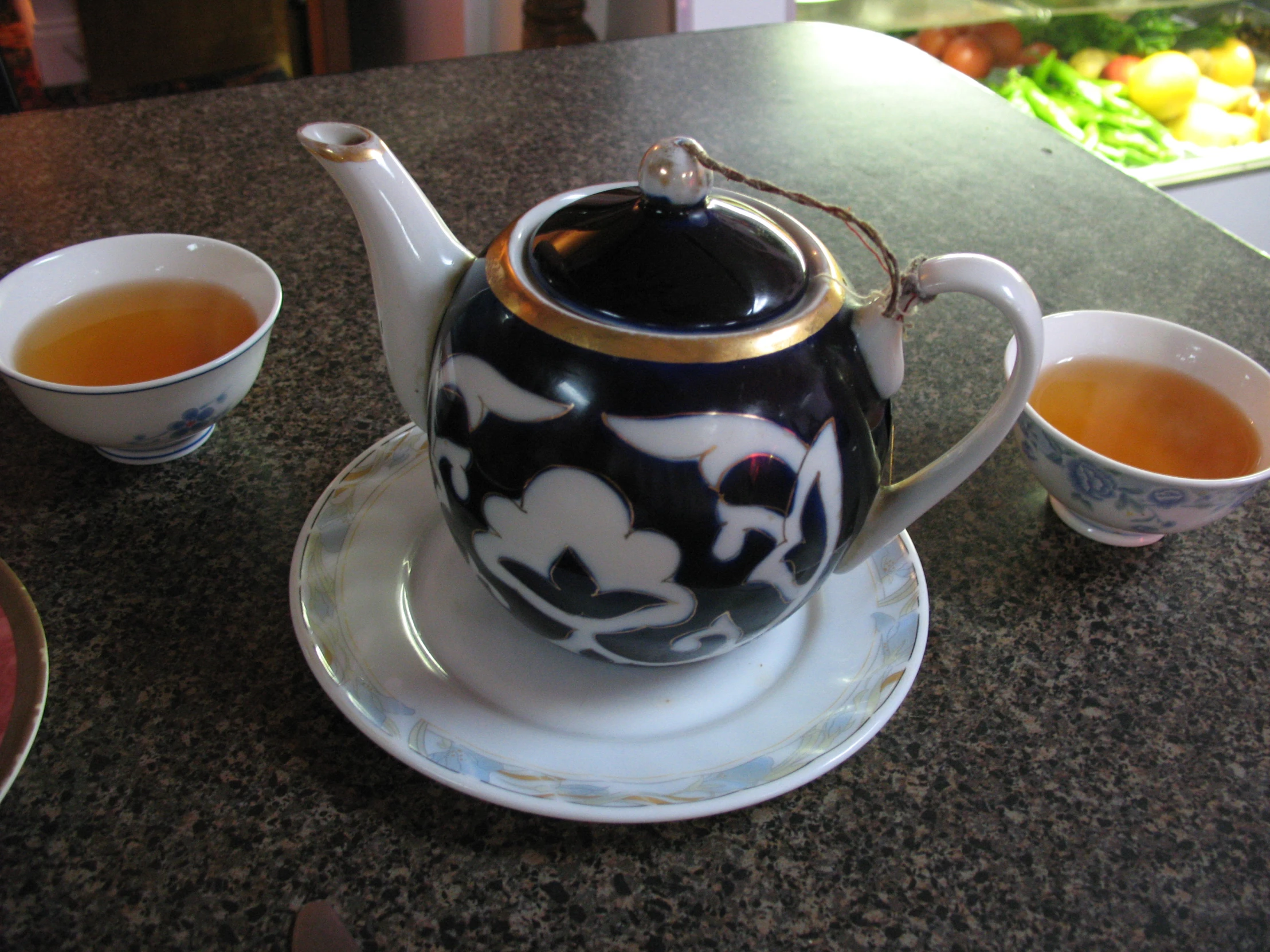 two cups with black flowers in them and a teapot with gold trimming on top