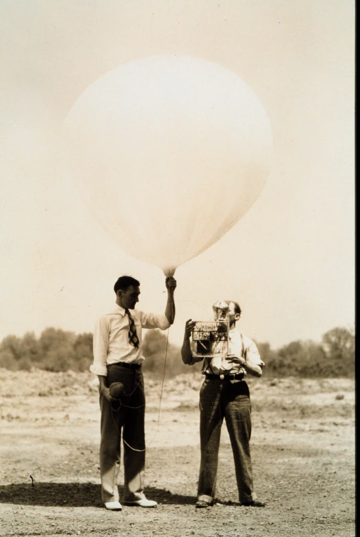 two men are in the desert and holding onto a large white ballon