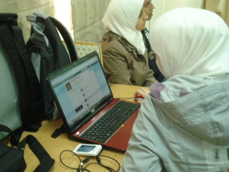 two women in hijabs are using laptops