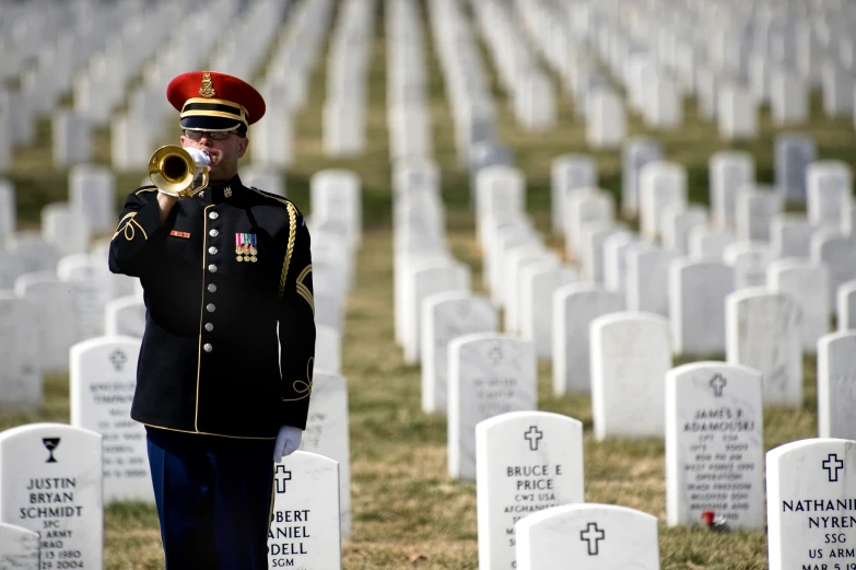 a military soldier in uniform plays a ss trombone near graves