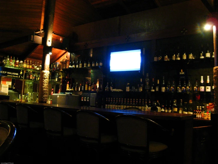 the bar in the dimly lit restaurant has a large television on the wall