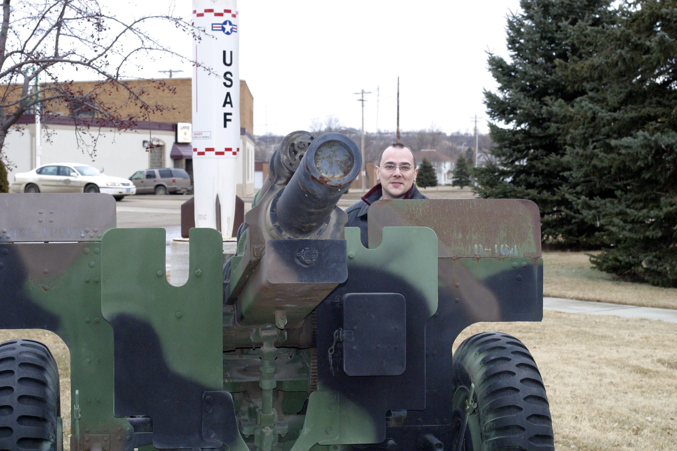 an old man poses behind a military vehicle