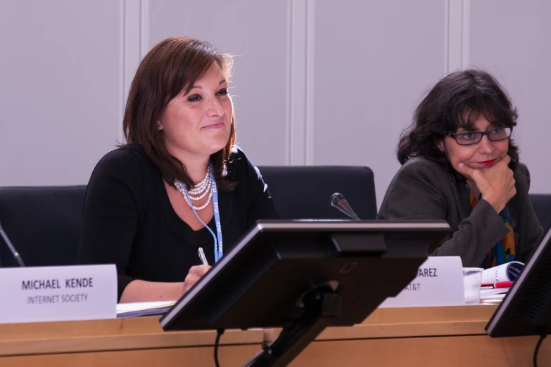 two women are sitting at a table with laptops