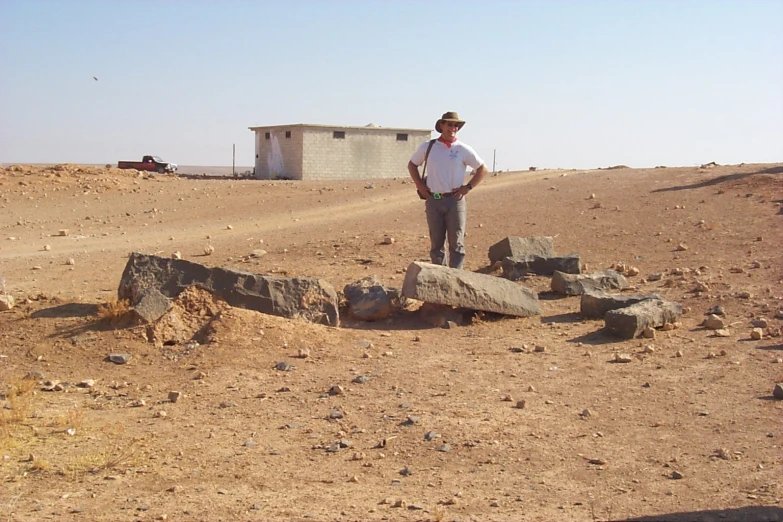 a man in a white shirt standing on rocks in the dirt