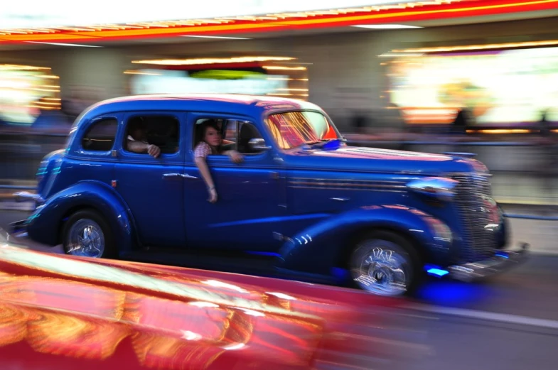 a close up of a blue old fashioned car driving down a street