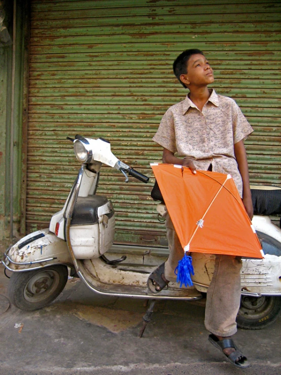 a boy standing next to his motorcycle with a kite on top