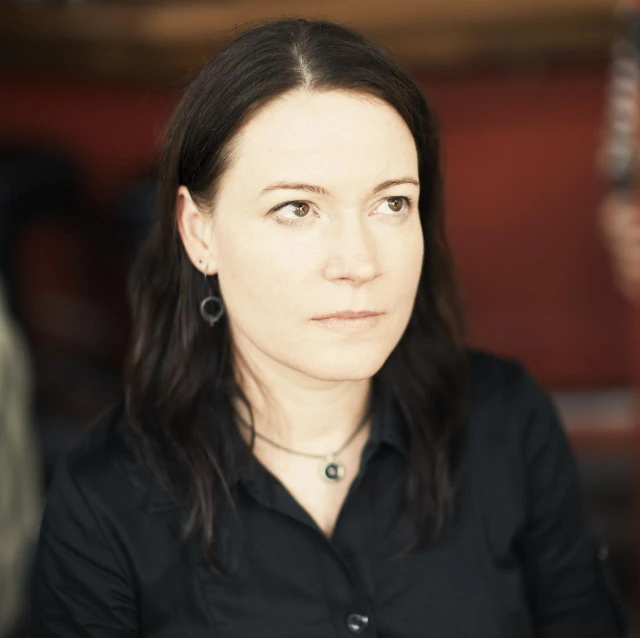 a woman with long black hair in a black shirt looks directly into the camera