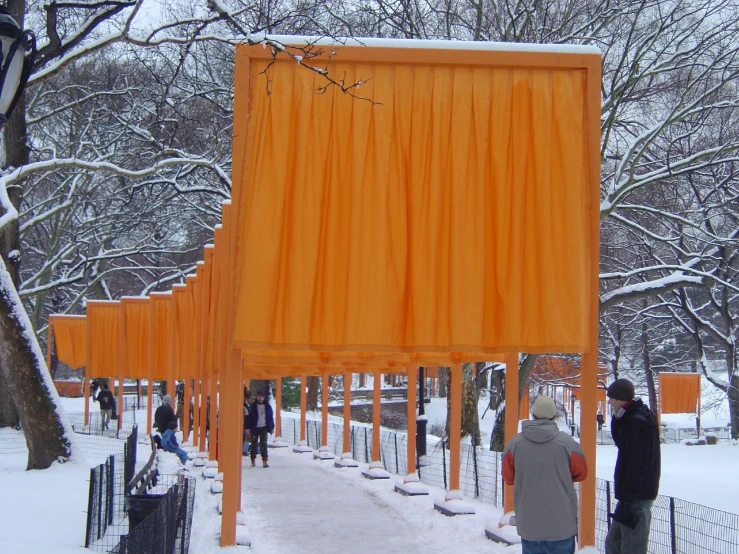 people walk through the snow in a park with a sculpture made of orange cloths