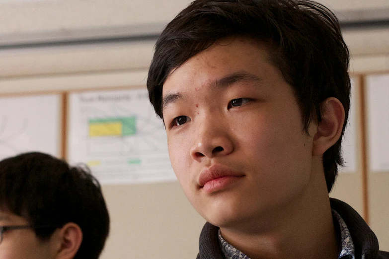 asian boy staring ahead while another man looks on