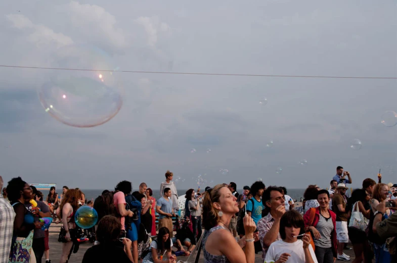 people gathered on a sidewalk as a kite flies overhead