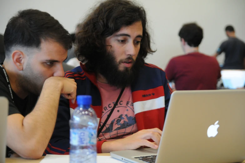 a pair of men sitting together working on their laptops