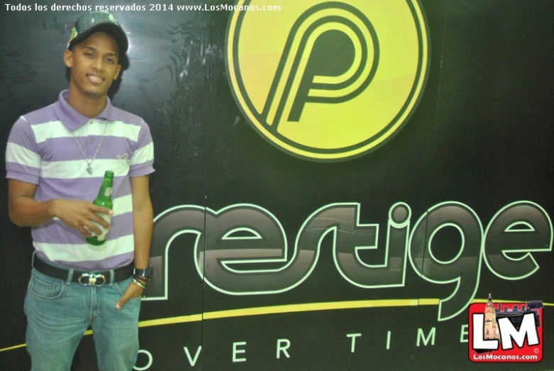 there is a young man standing by a sign and holding onto a green beer bottle