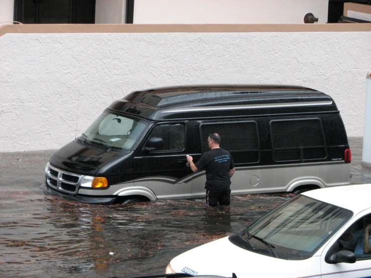 a man stands in flood water as his van goes under water