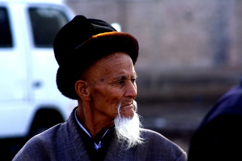 an older man with a hat and beard stares straight ahead