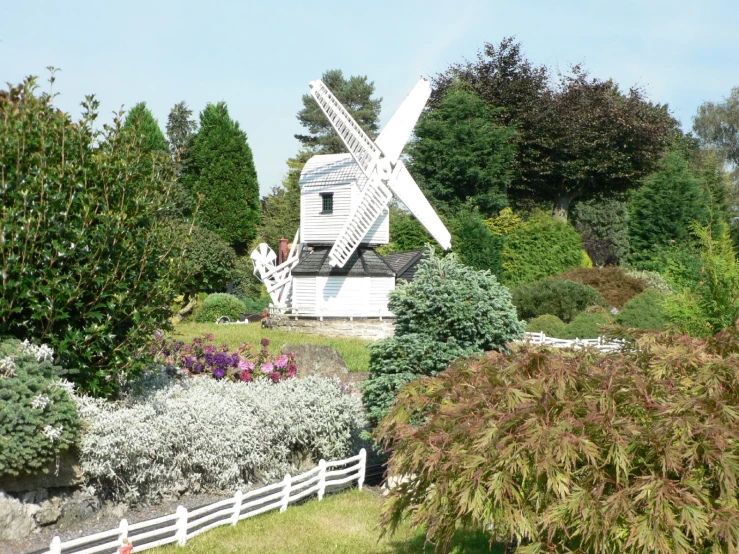 a windmill and trees are shown near a white fence