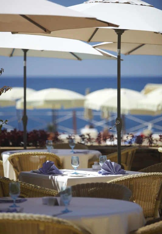 tables are set up under umbrellas with the sea in the background