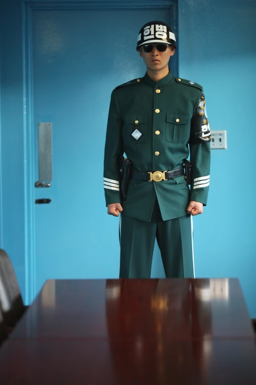 a uniformed man standing at a table in front of blue wall