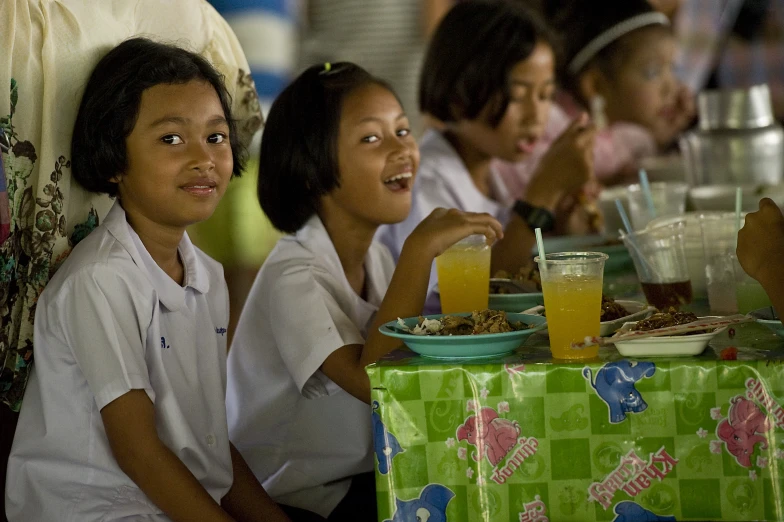 a group of children smiling while eating and drinking juice