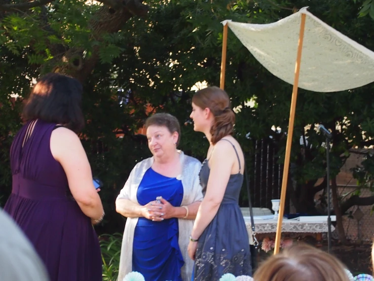 two women wearing dresses talk under an umbrella