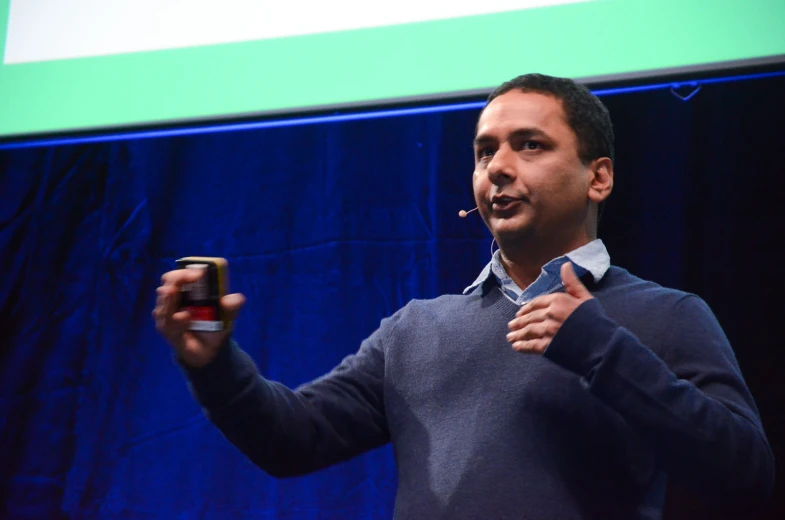 a man in blue sweater holding up his hand while giving a presentation