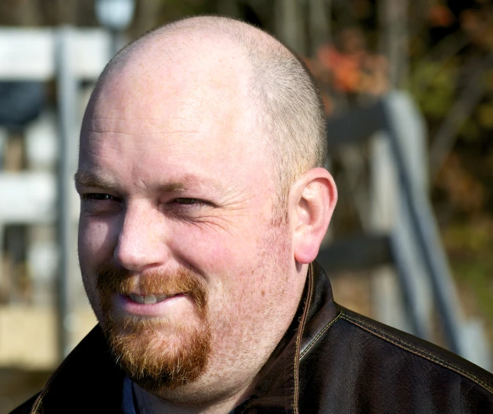 a bald man with a brown jacket smiles into the camera