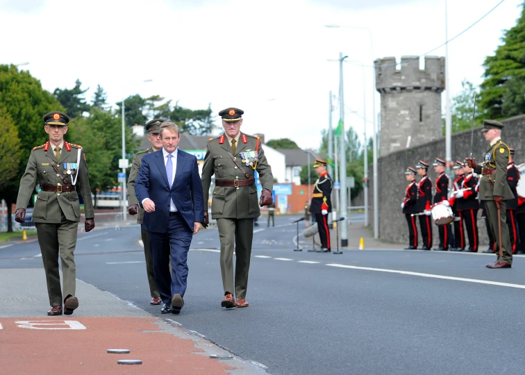 two men in suits walk in front of other uniformed military personnel