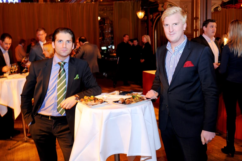 a couple of men in suits and ties standing next to table